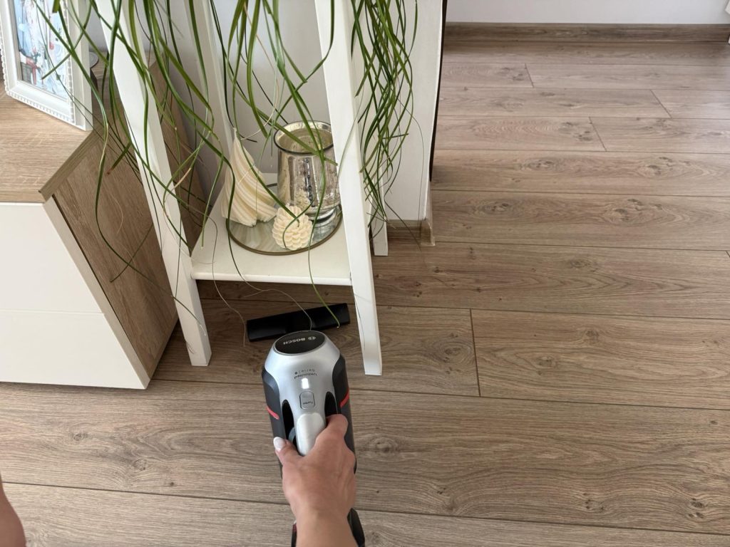 Vacuuming a wooden floor beside a cabinet and plant